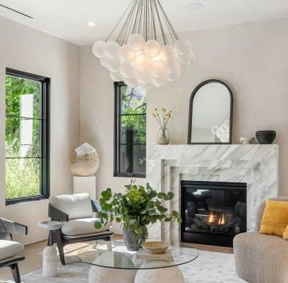 Modern living room with elegant chandelier, marble fireplace, and stylish decor, featuring a glass table and cozy seating.
